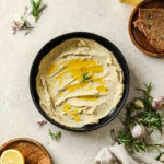 white bean dip with rosemary in black bowl on beige background.