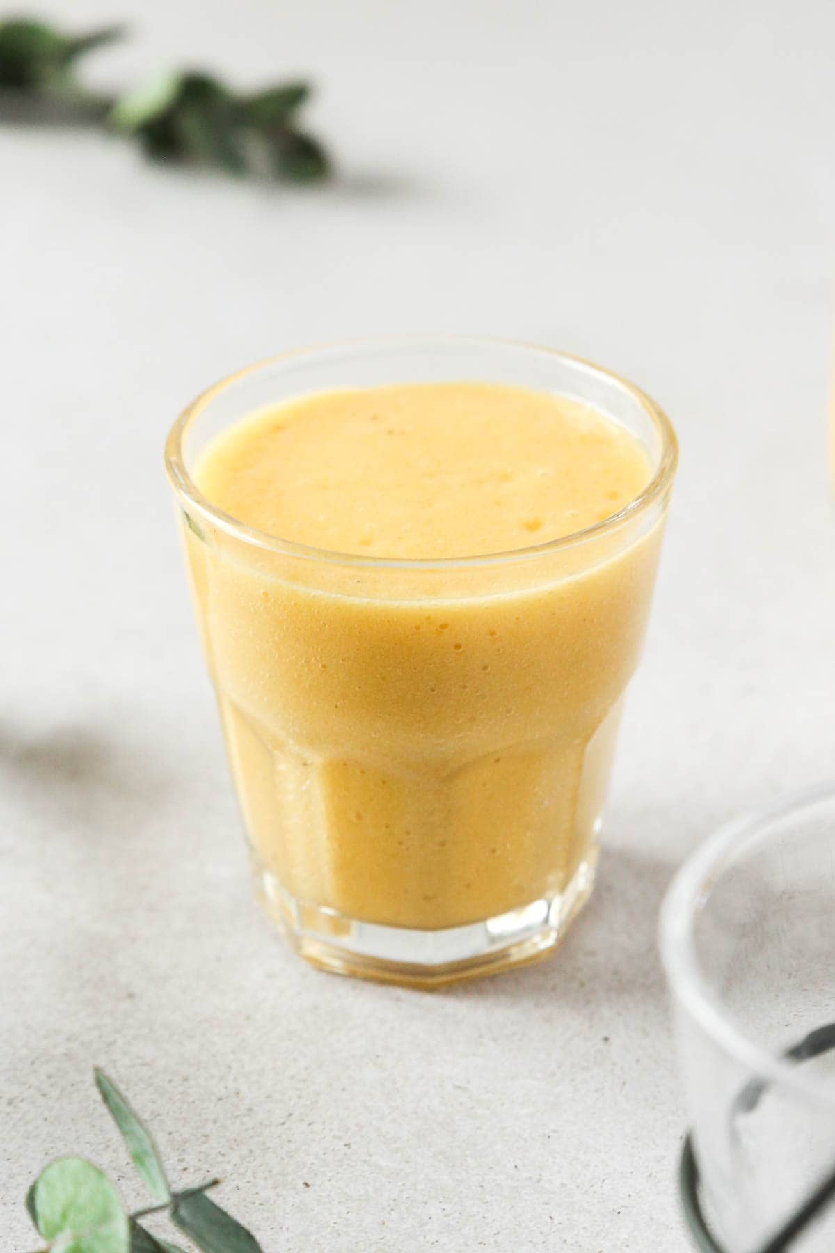 vegan tropical mango banana smoothie in glass on grey background with props.