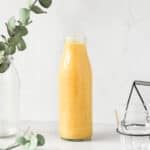 tropical mango banana smoothie in glass bottle on grey background with props.