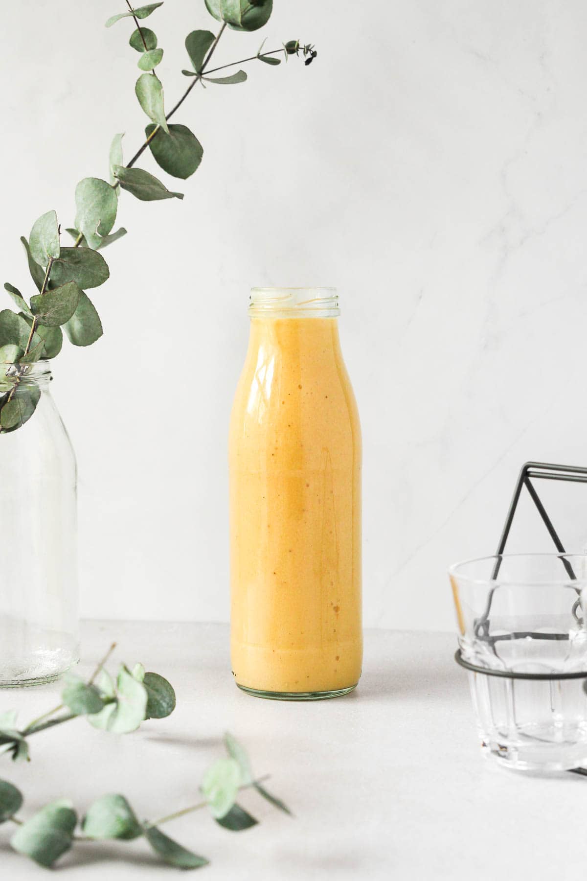 tropical mango banana smoothie in glass bottle on grey background with props.